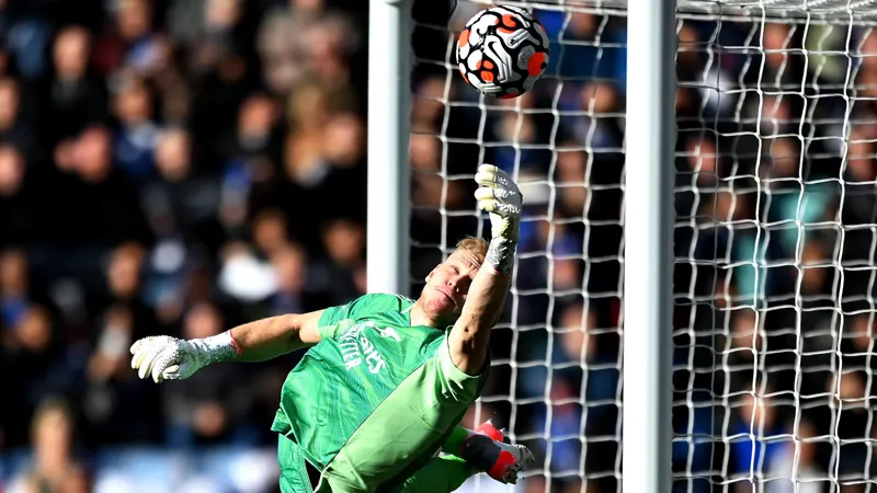 A goalkeeper in green diving to save a ball at the goal